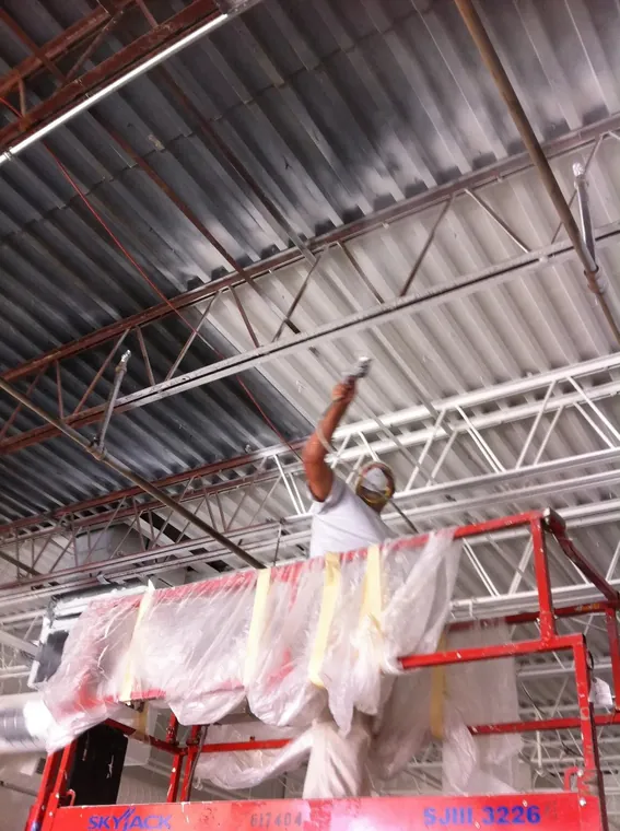 Spray-painting an industrial warehouse ceiling from a scissor lift